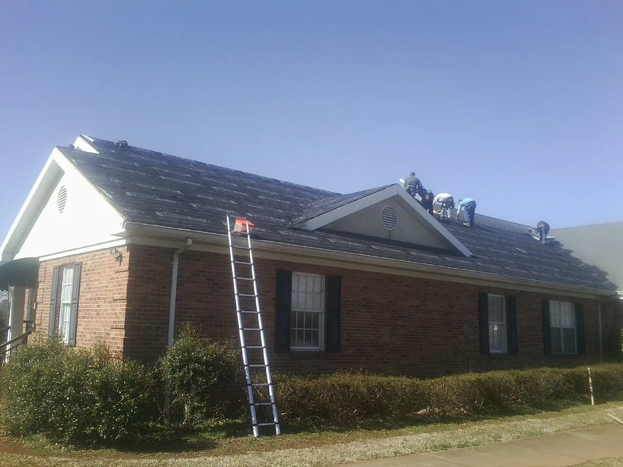 Crew tearing shingles off a brick ranch roof with a ladder set — Metal Roof Repair work by our crew in Sheffield