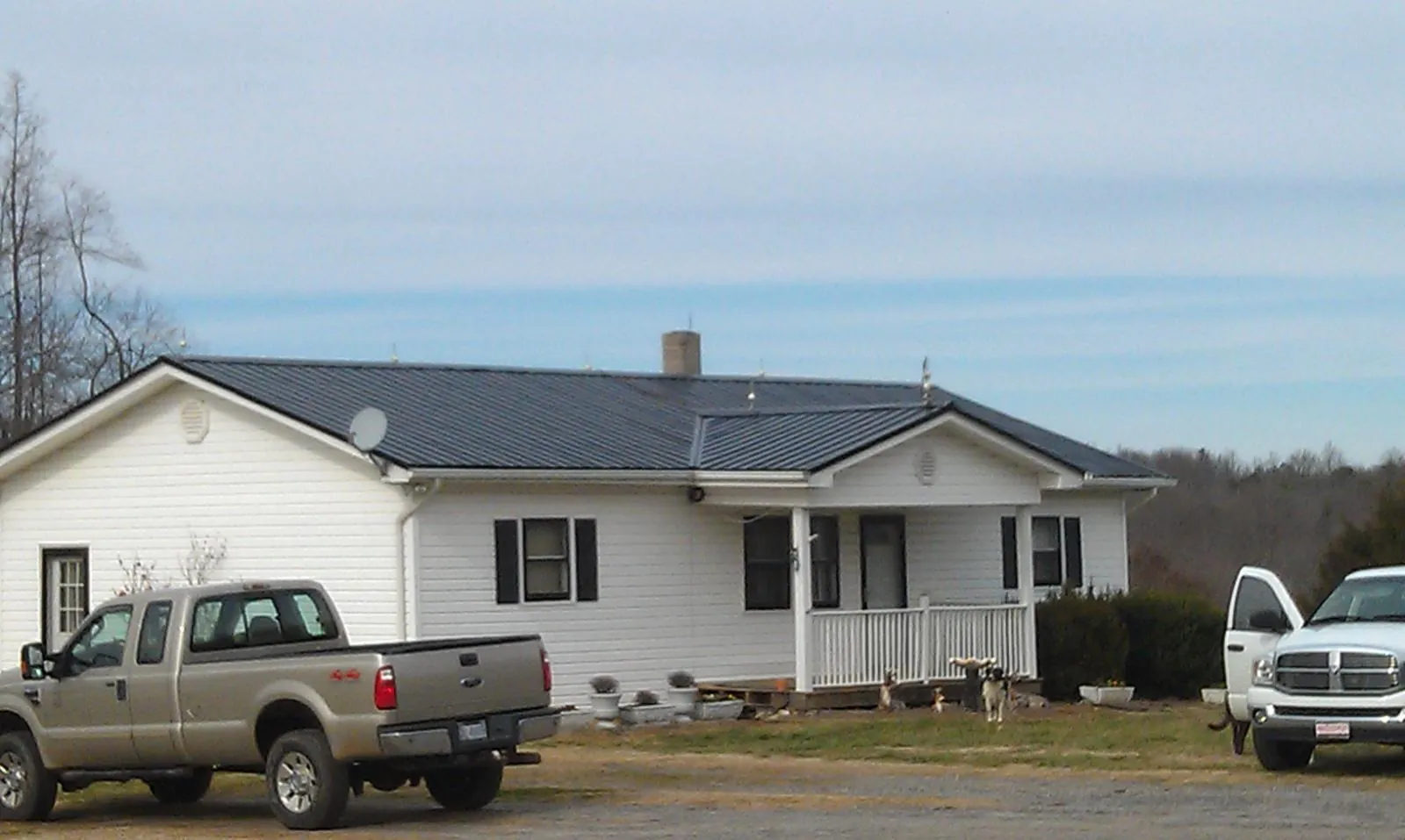 Finished dark metal roof on a white ranch home with work trucks parked in Sheffield